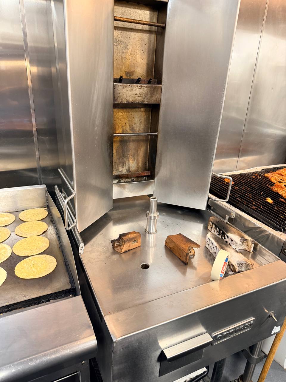 Vertical cooking equipment beside a griddle and charbroiler